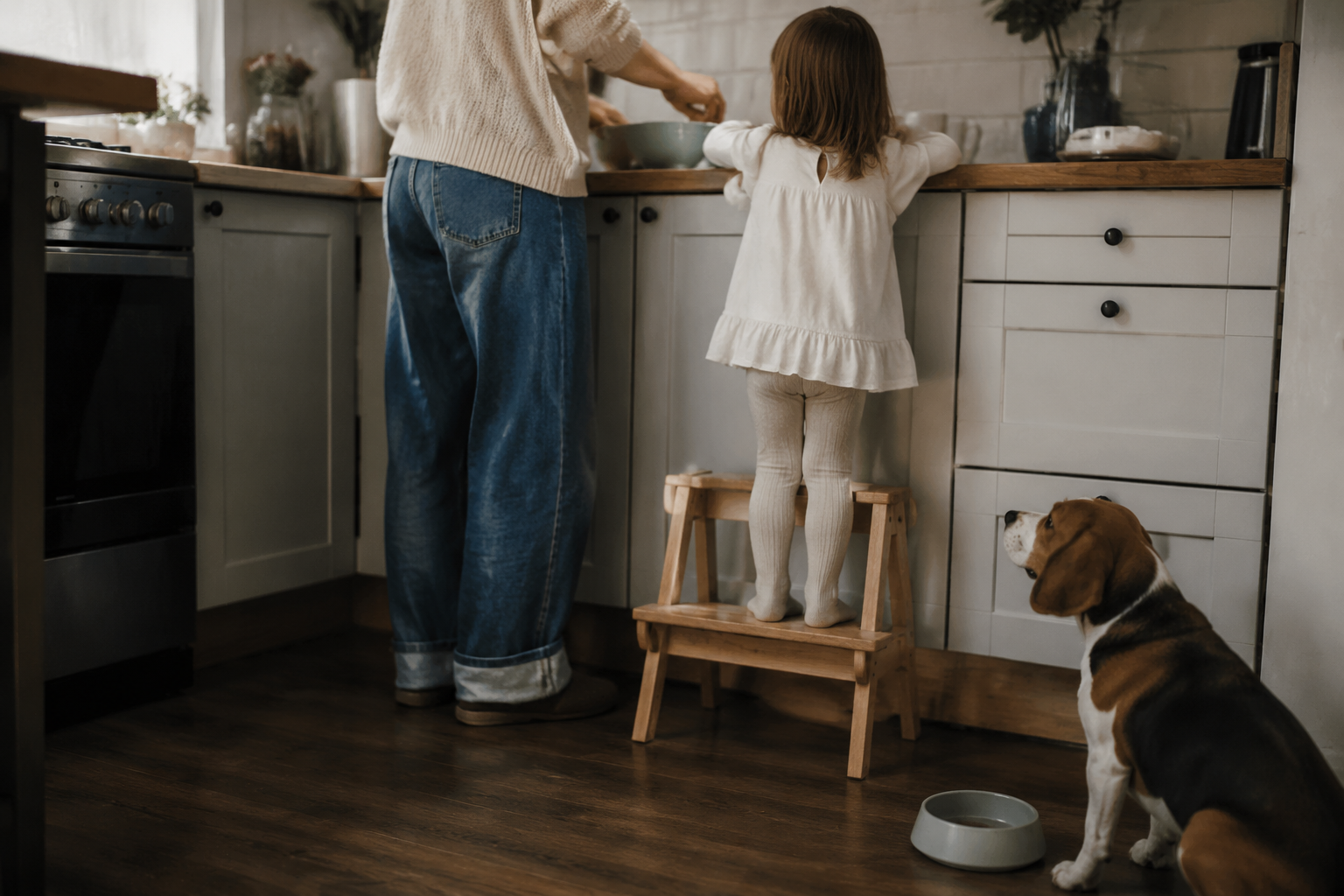 A parent and young child cooking together with their Beagle's empty bowl on the kitchen floor
